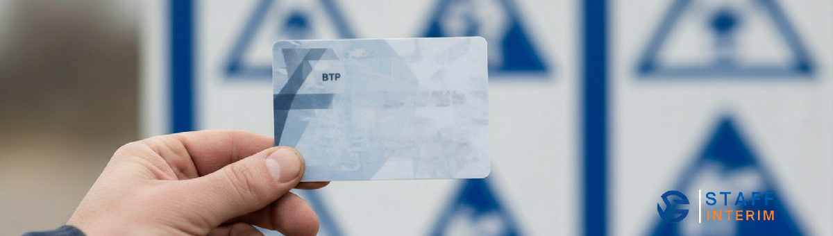 Main tenant une carte BTP devant un panneau de chantier.